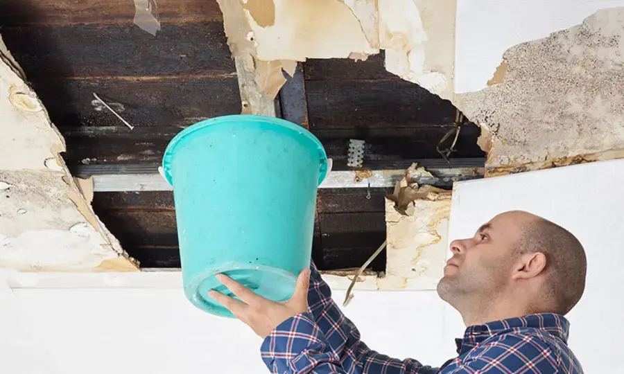Homeowner holding a bucket under an opened ceiling after a roof leak in El Monte